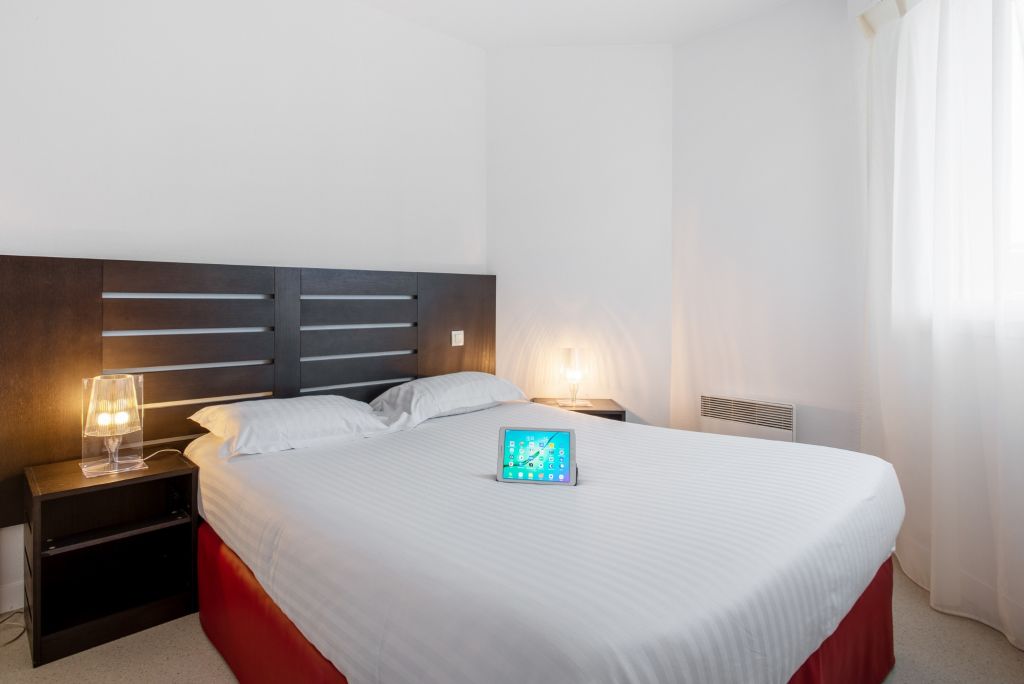 Chambre Appartement T2 avec une tablette posée sur le lit - appart hotel le liberte vannes